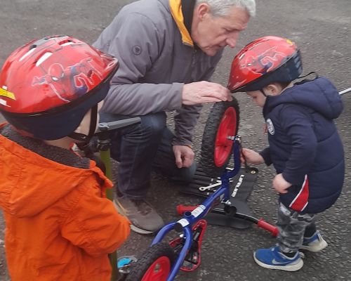 Older man looking at a balance bike upside down with two toddlers